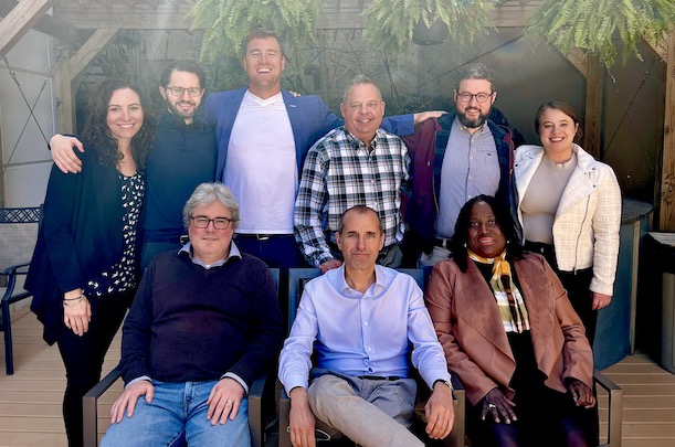 6 people standing with three people sitting in front