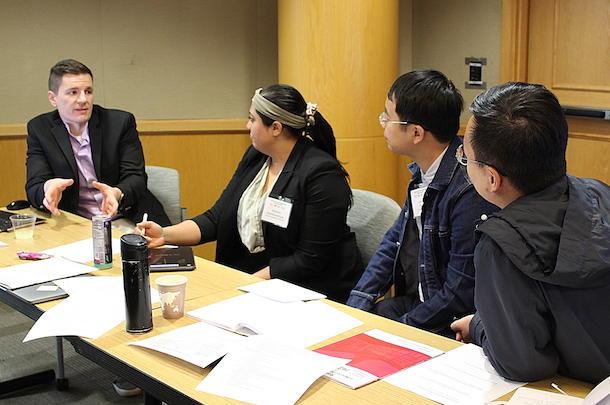 Three participants speak with faculty member seated at table