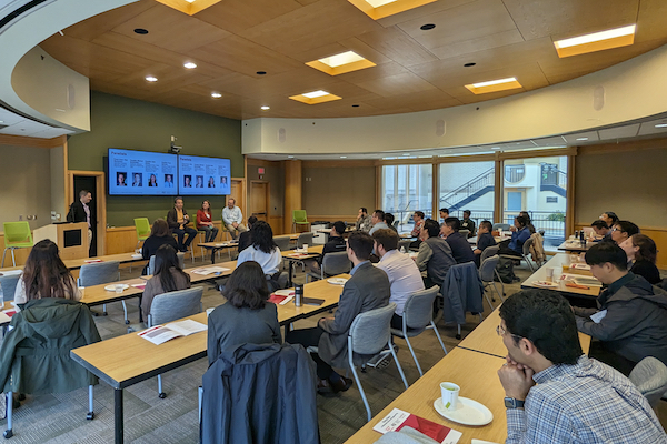 Presenters seated at front of room with participants sitting at tables