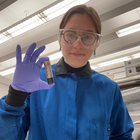 Hannah Morin in lab coat holding a battery