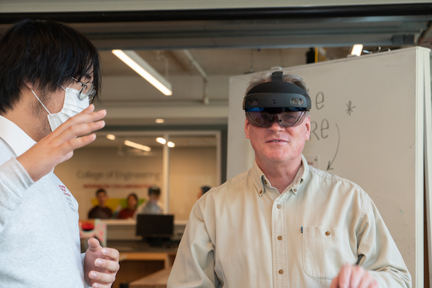 Person wearing AR goggles standing next to student